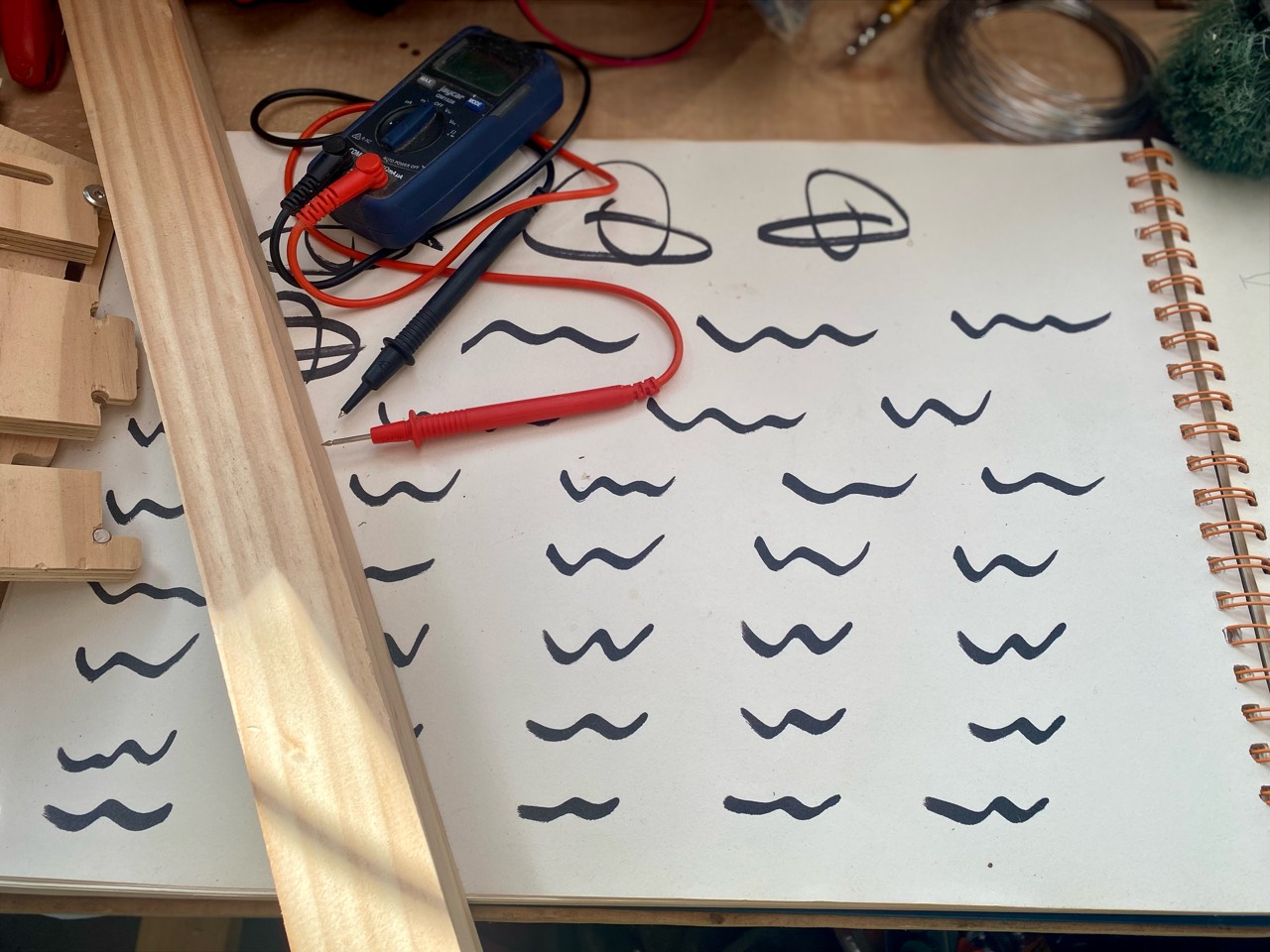 Electrical probes and timber pieces laid over a sketchbook of hand-drawn marks.
