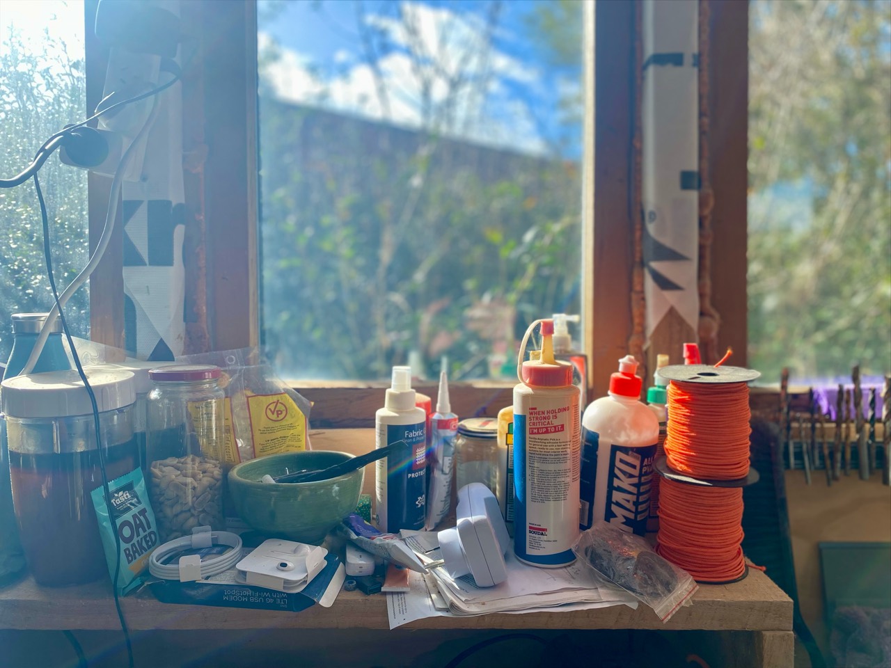 Glue, cord, brushes, and small components gathered beside a sunlit workshop window.