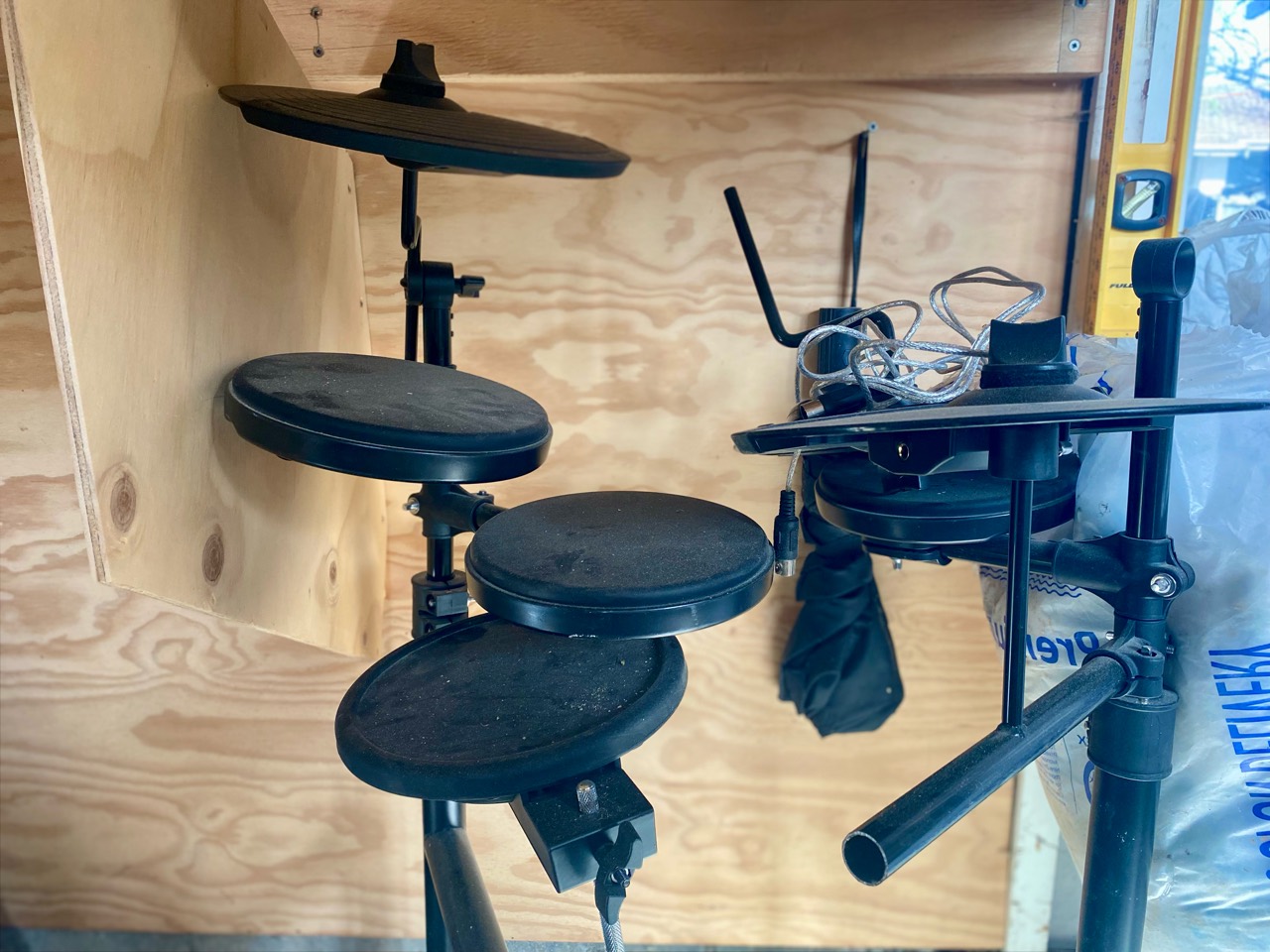 Electronic drum pads and stands stored against a plywood wall.